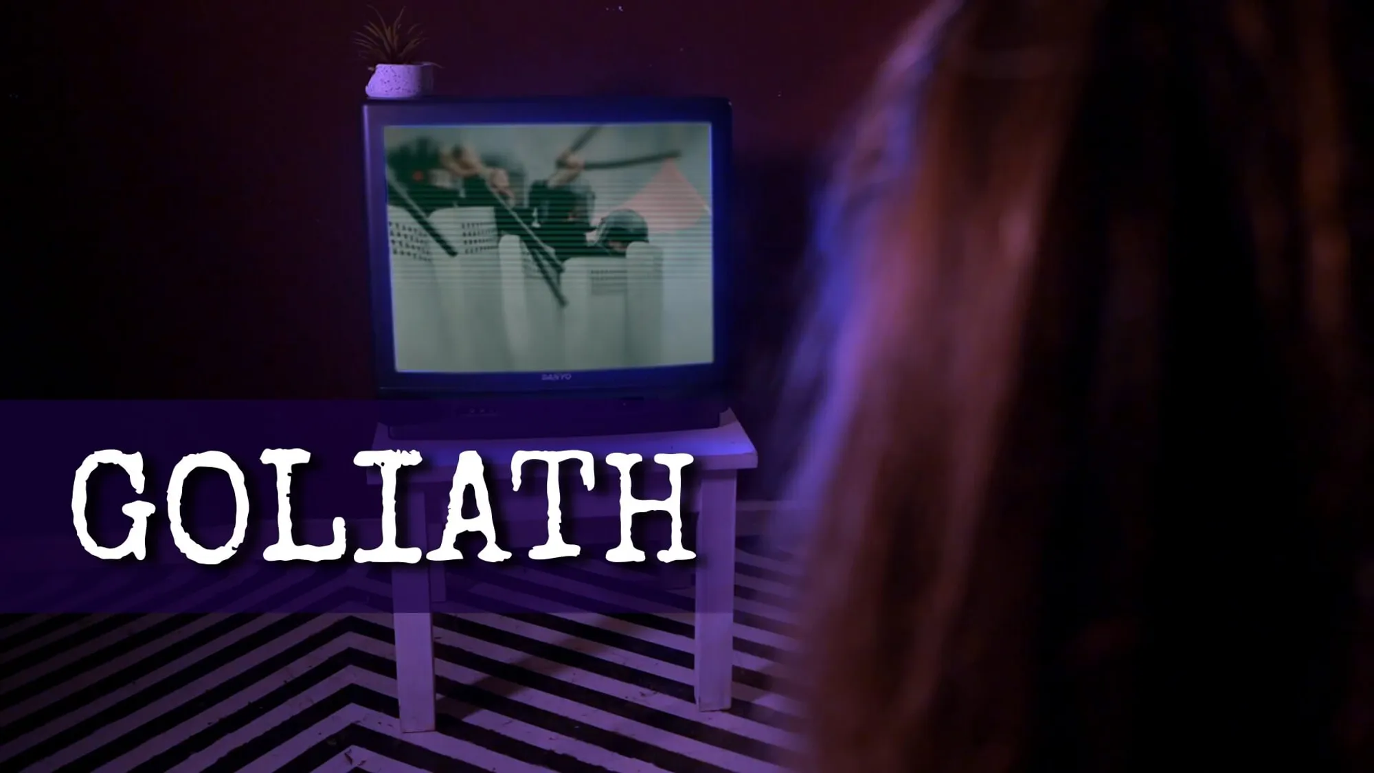A person watches TV with some bad news on. Goliath is written at the bottom.